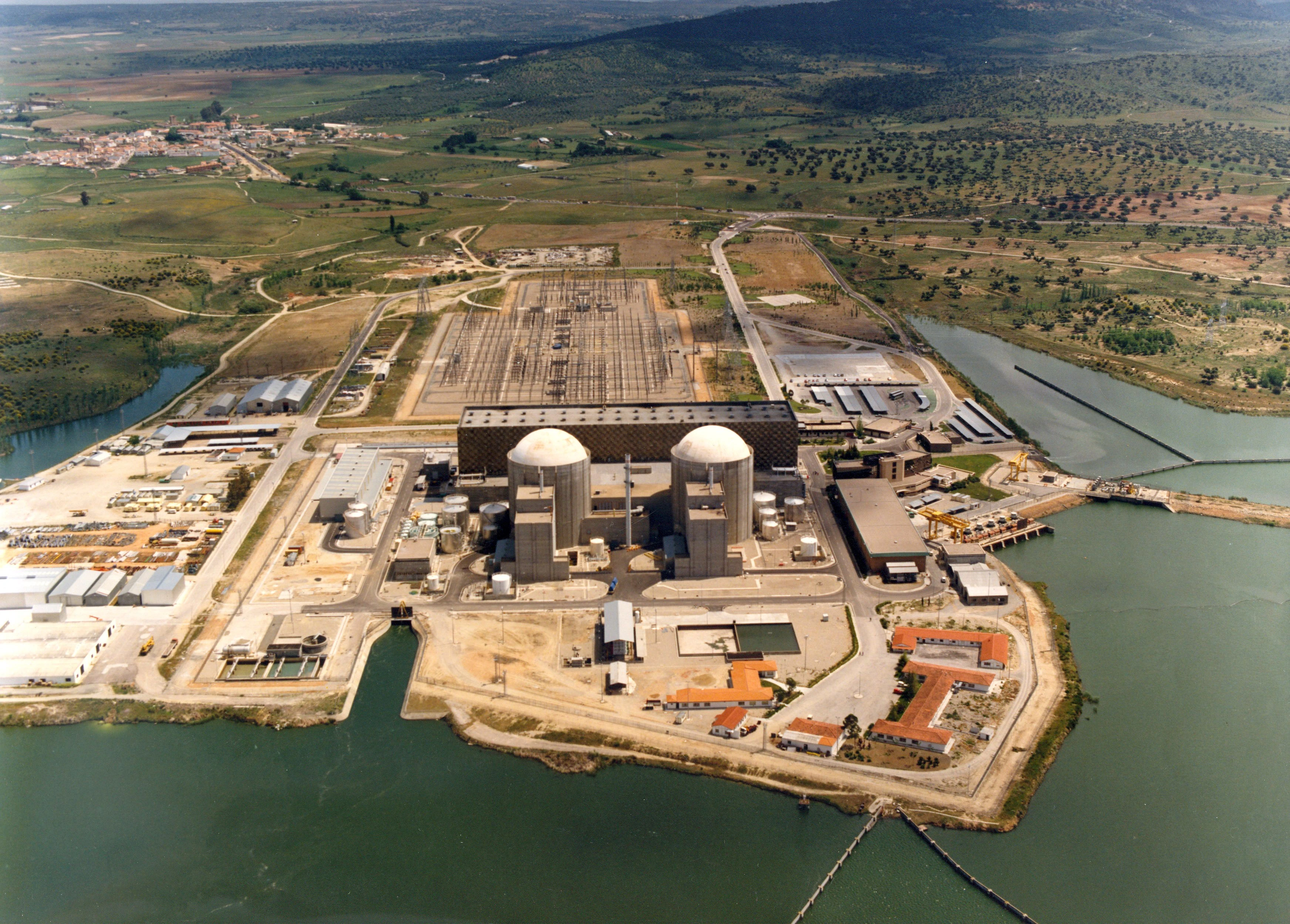Vista aérea de una planta nuclear junto a un río, con dos grandes reactores y una subestación eléctrica