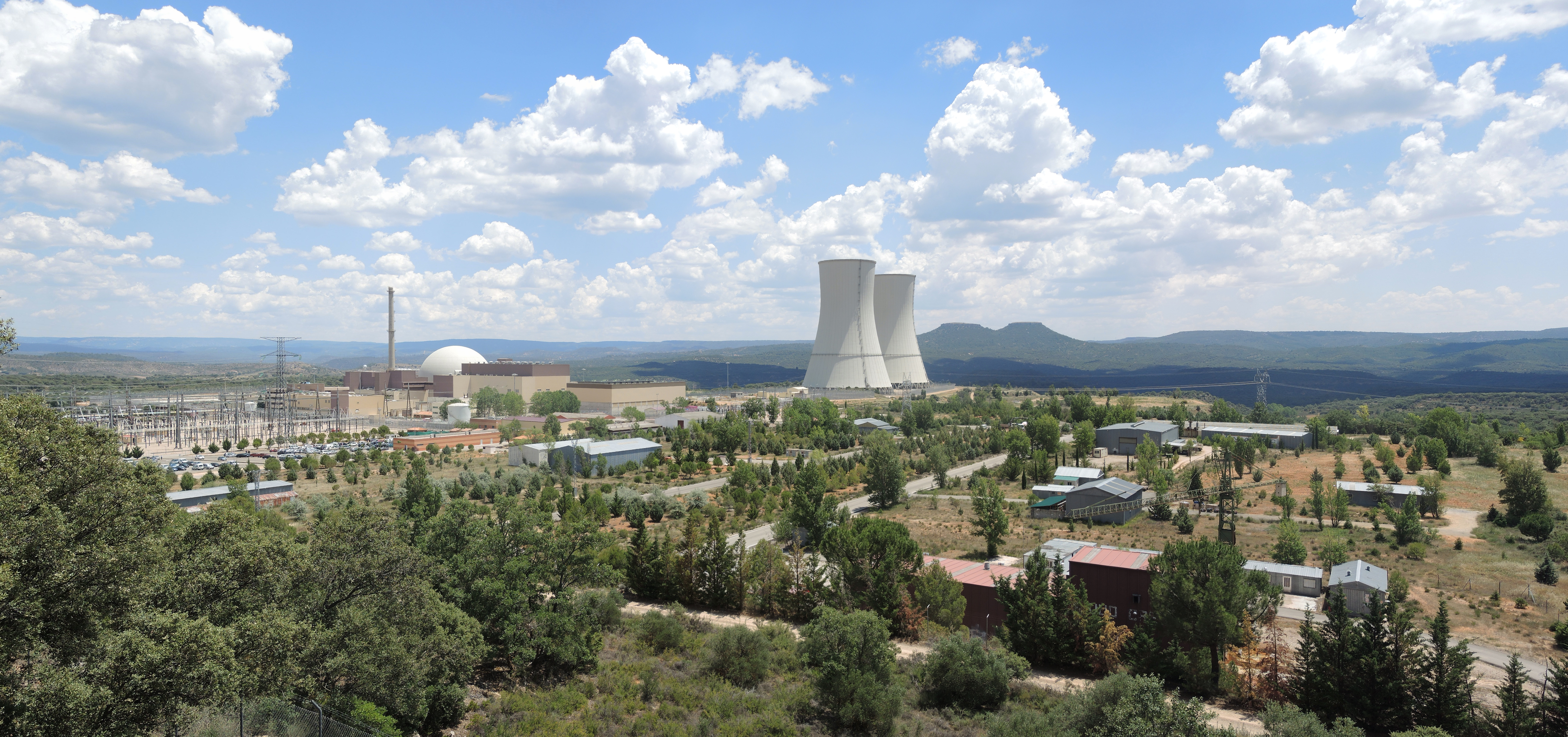 Vista panorámica de una planta nuclear con torres de refrigeración, subestación eléctrica y entorno montañoso.