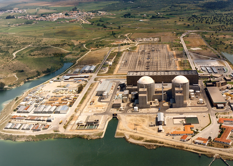 Vista aérea de una central nuclear junto a un río, con torres de contención y varias instalaciones industriales rodeadas de campos y colinas.
