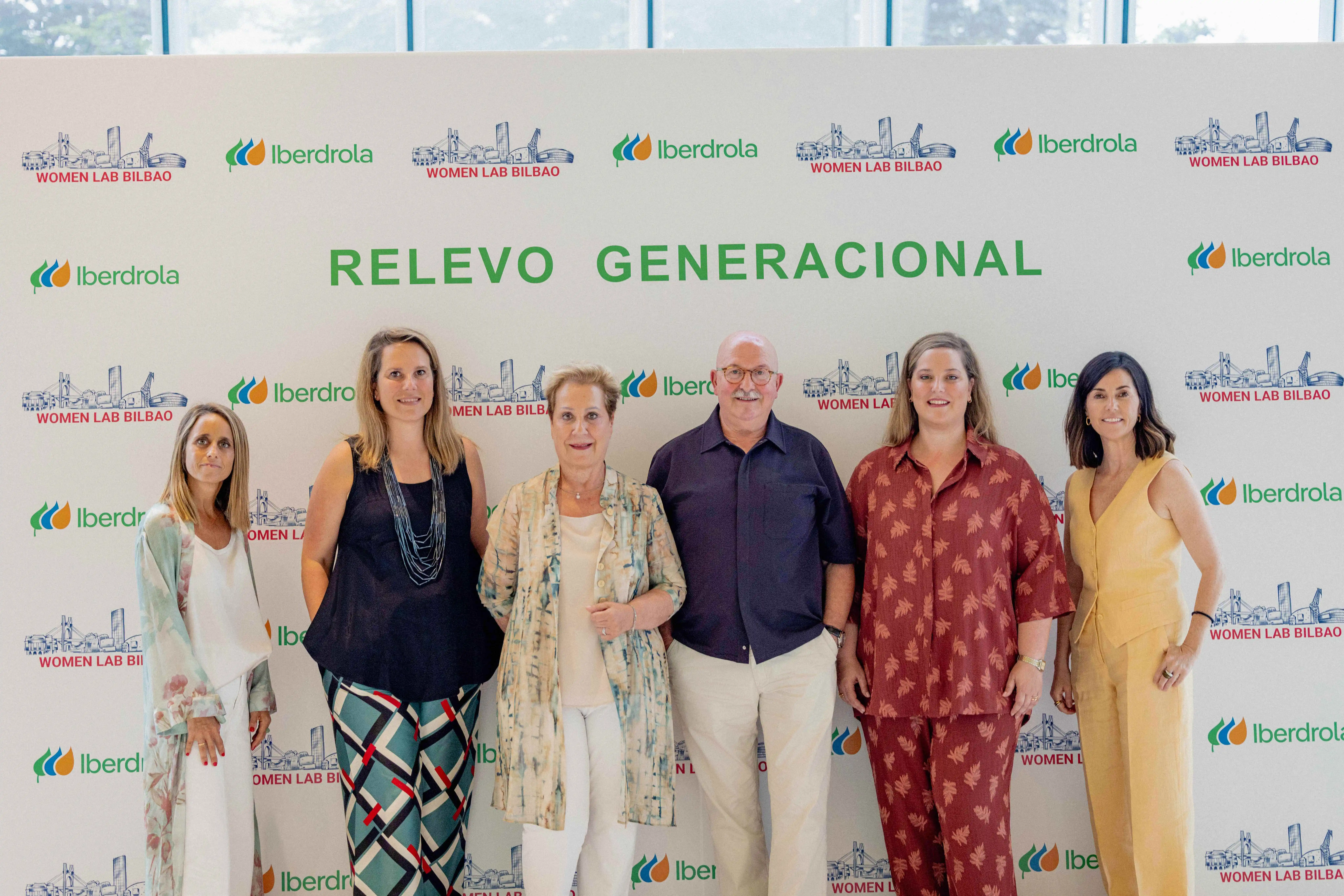 Grupo de personas posando frente a un fondo con logotipos de Iberdrola y Women Lab Bilbao, con un cartel que dice "Relevo Generacional". Hay cinco adultos (tres mujeres y dos hombres) alineados en primer plano, todos sonrientes, vestidos de manera formal y casual.