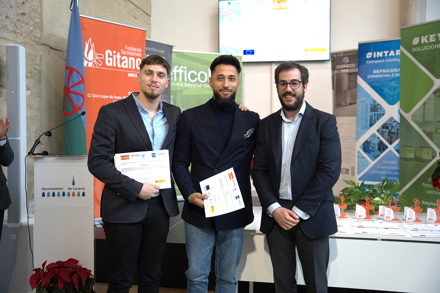 Tres hombres de pie, sonriendo, dos de ellos sosteniendo certificados del programa educativo