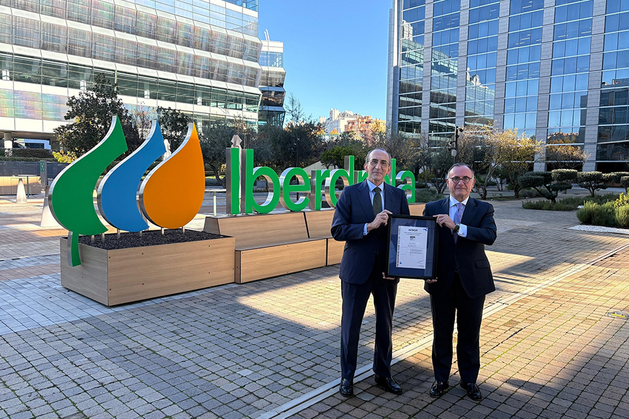 Foto de dos personas sosteniendo un certificado frente al logo de Iberdrola en el exterior de un edificio