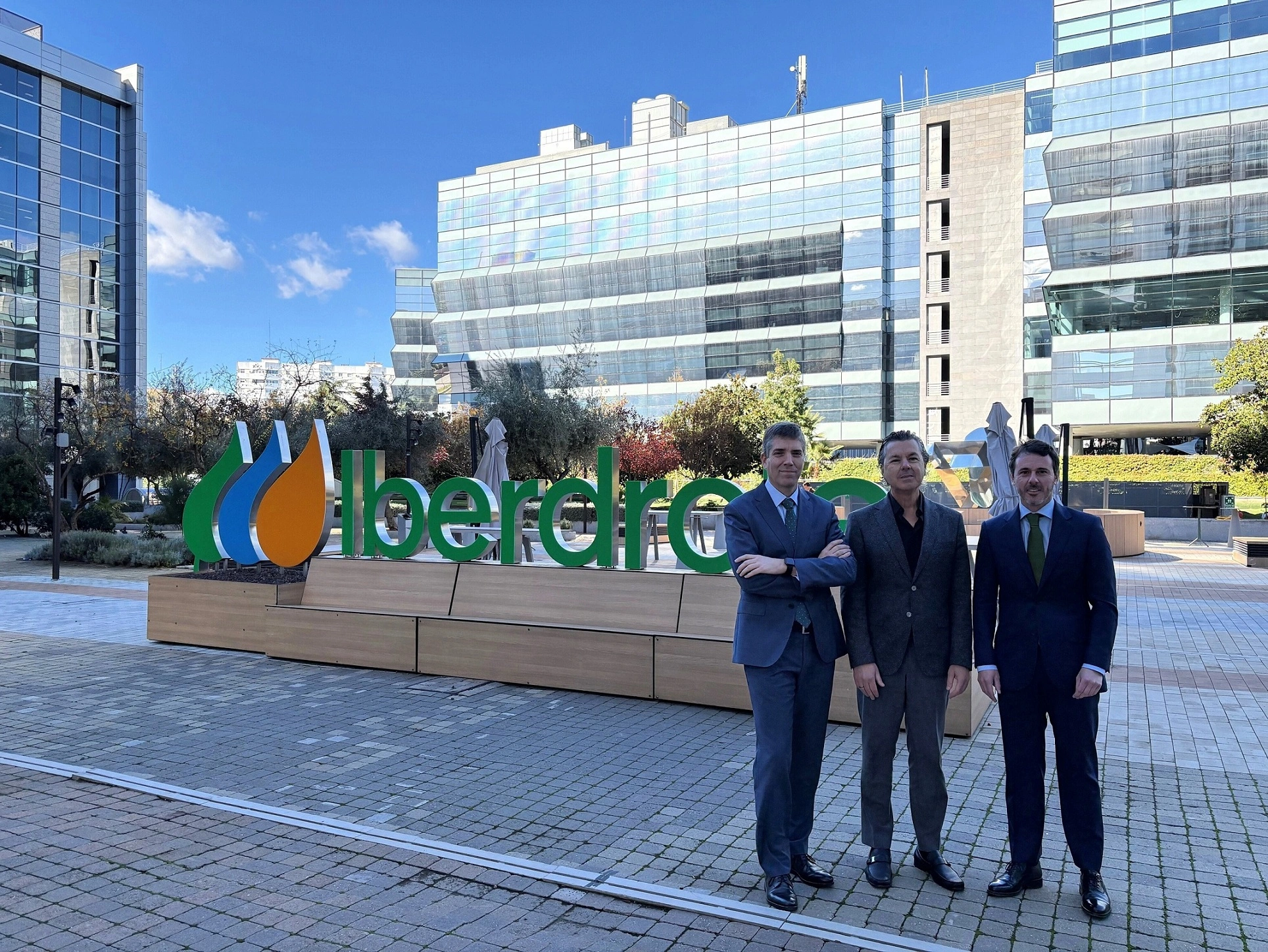Tres personas posan frente a la sede de Iberdrola, con el logo de la empresa claramente visible en el fondo.