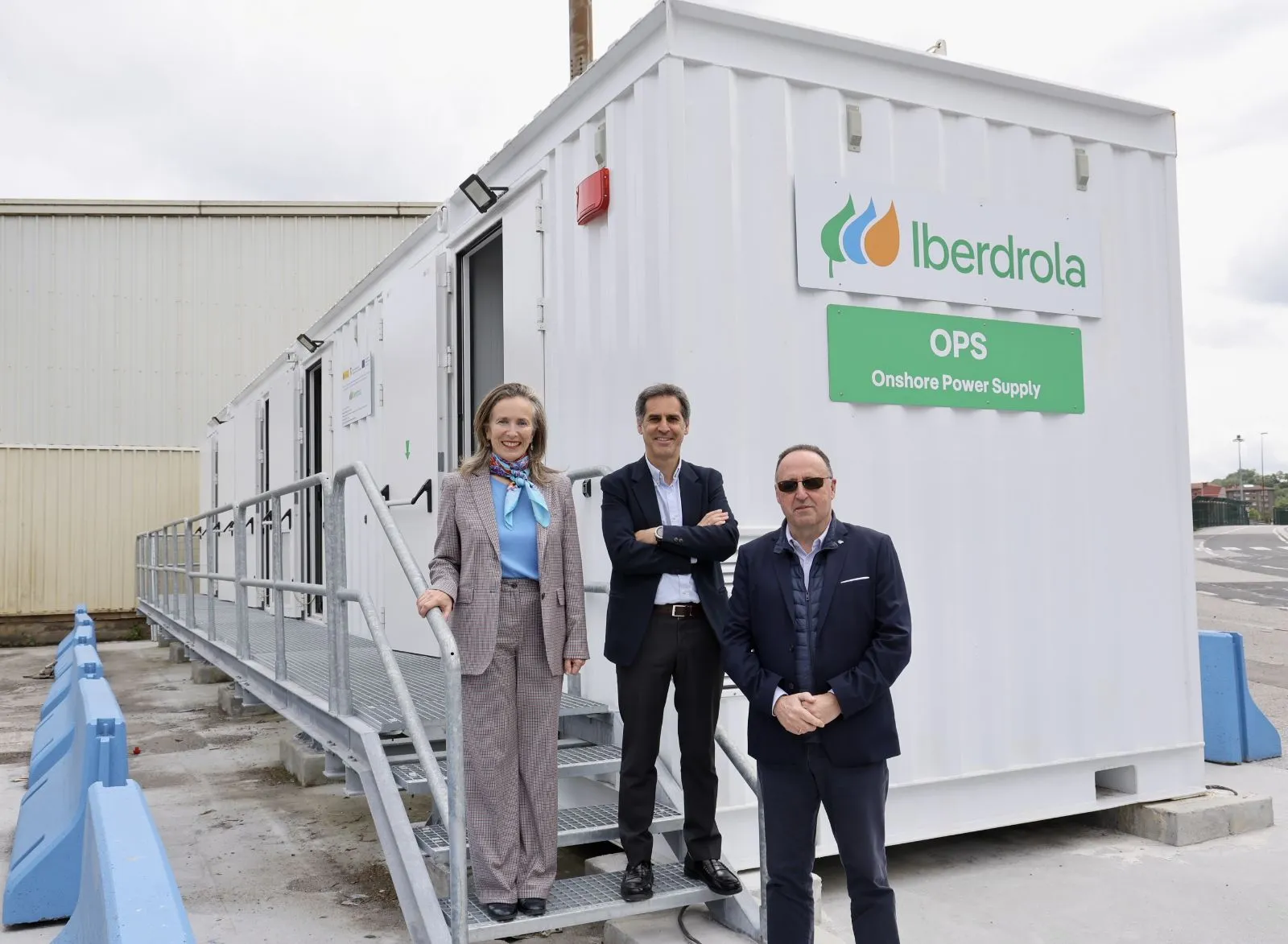 Tres personas posando frente a un contenedor de Iberdrola OPS (Onshore Power Supply) en un puerto industrial.