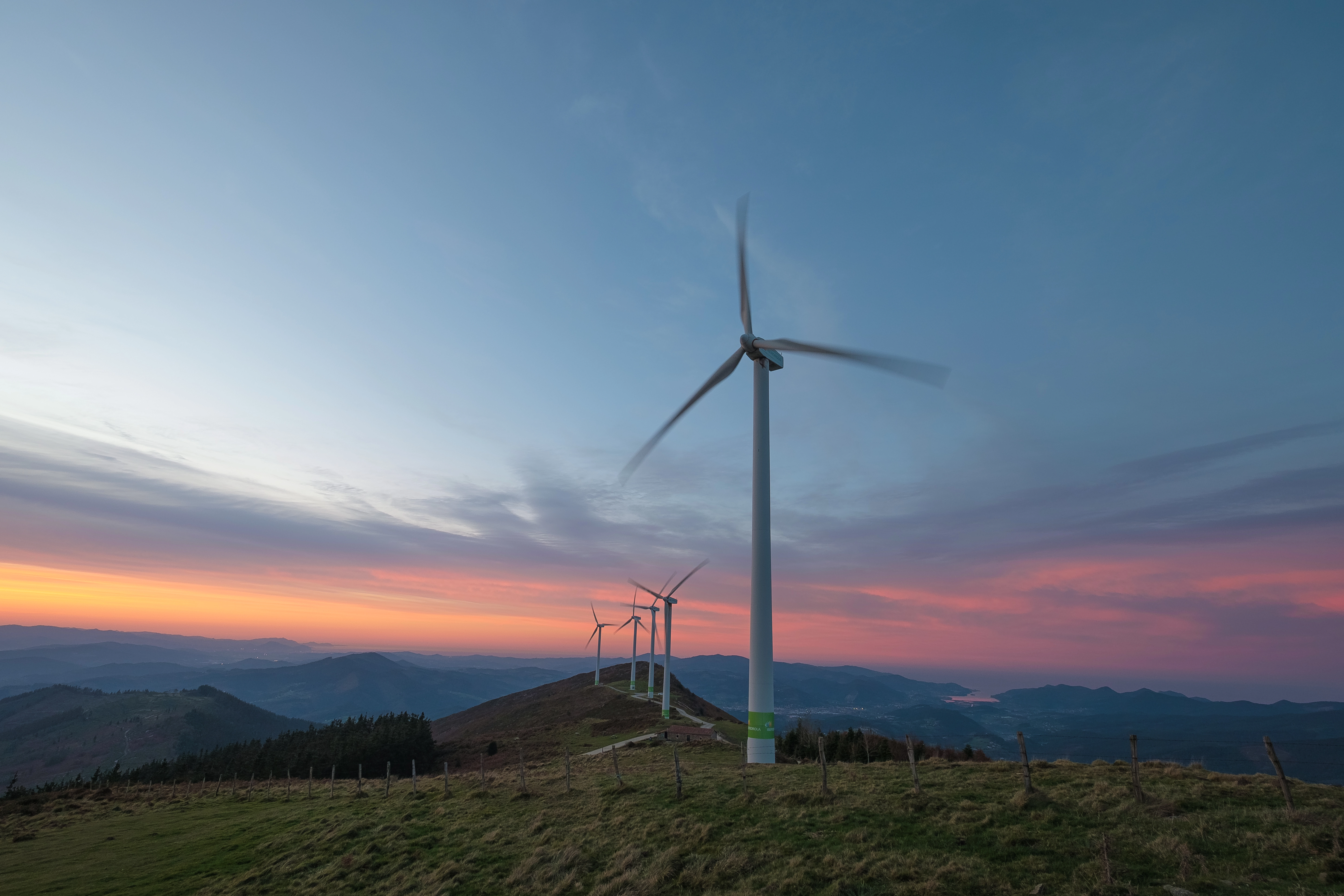 Aerogeneradores de Iberdrola España en una montaña al atardecer, con el paisaje iluminado por tonos azules y rosados.