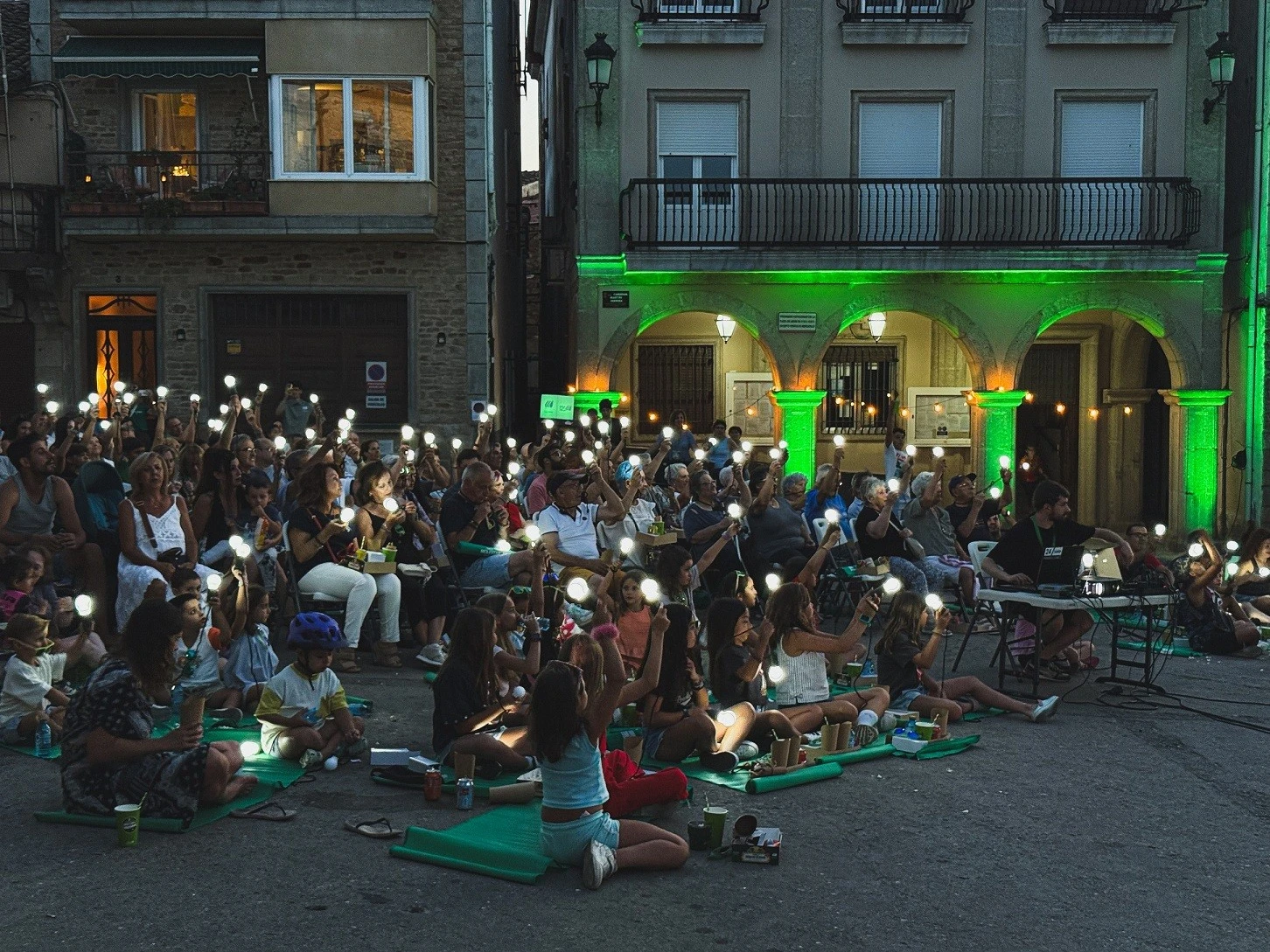 Público asistiendo a un evento nocturno con luces sostenibles en una plaza urbana.