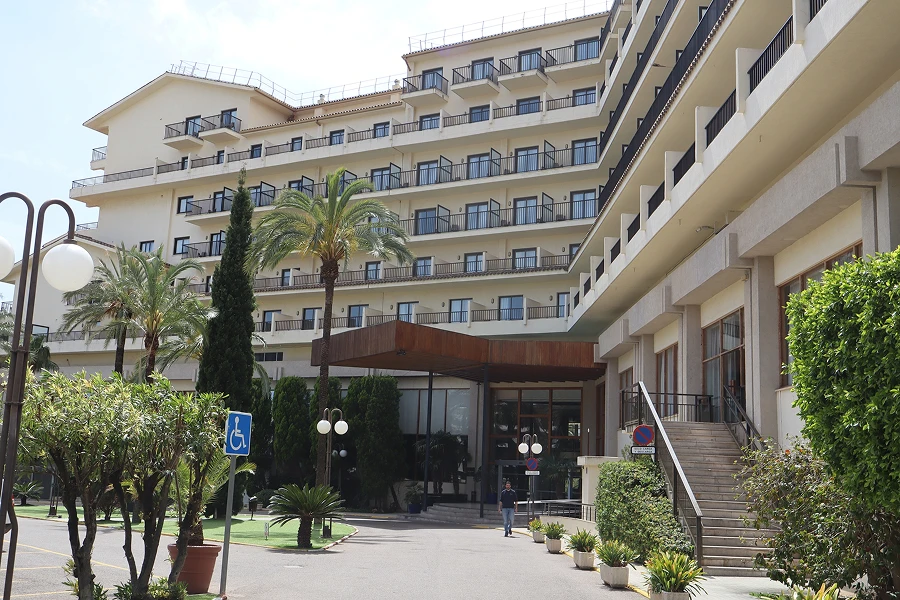 Vista exterior del Hotel Intelier Orange de Benicàssim, con un edificio de varias plantas y balcones, rodeado de palmeras y zonas ajardinadas junto a la entrada principal.