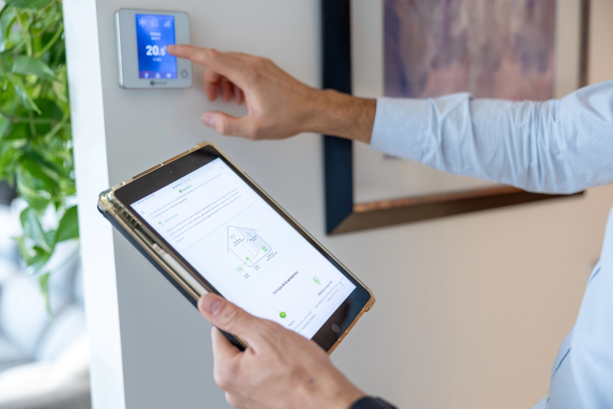 Persona ajustando la temperatura de un sistema de aerotermia mientras consulta información energética en una tableta.