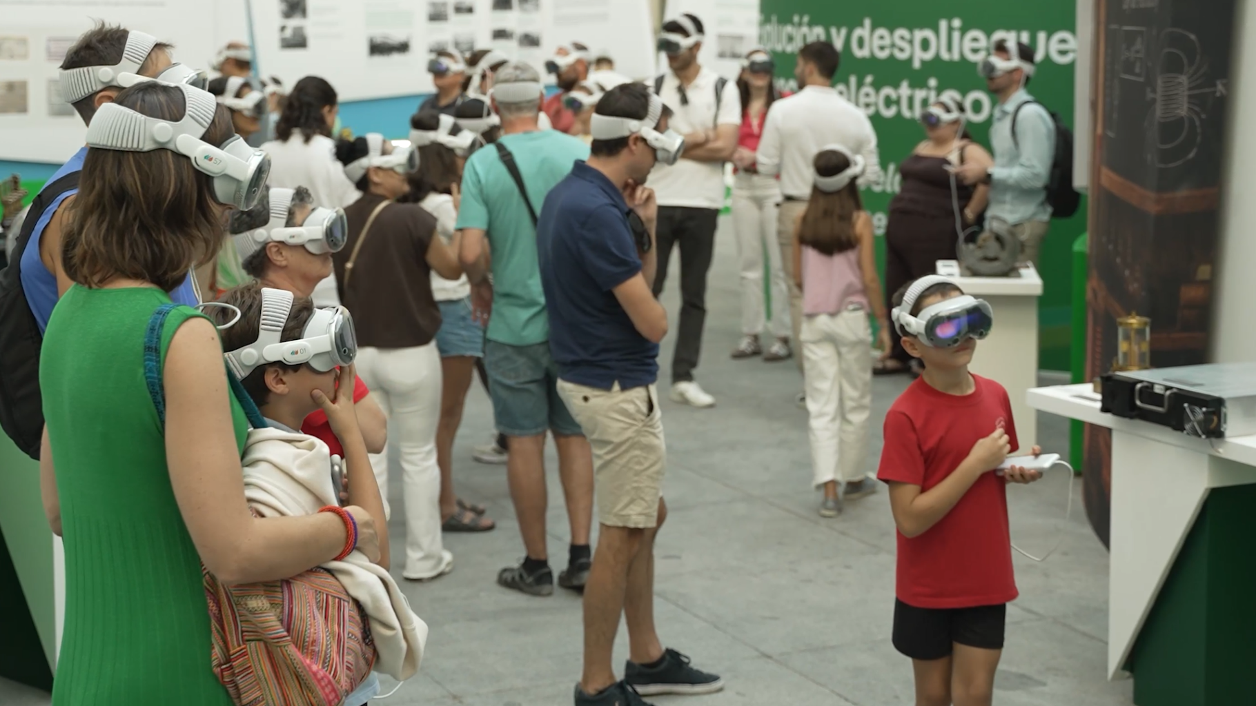 Adultos y niños utilizan gafas de realidad virtual en una exposición interactiva sobre electricidad y tecnología.