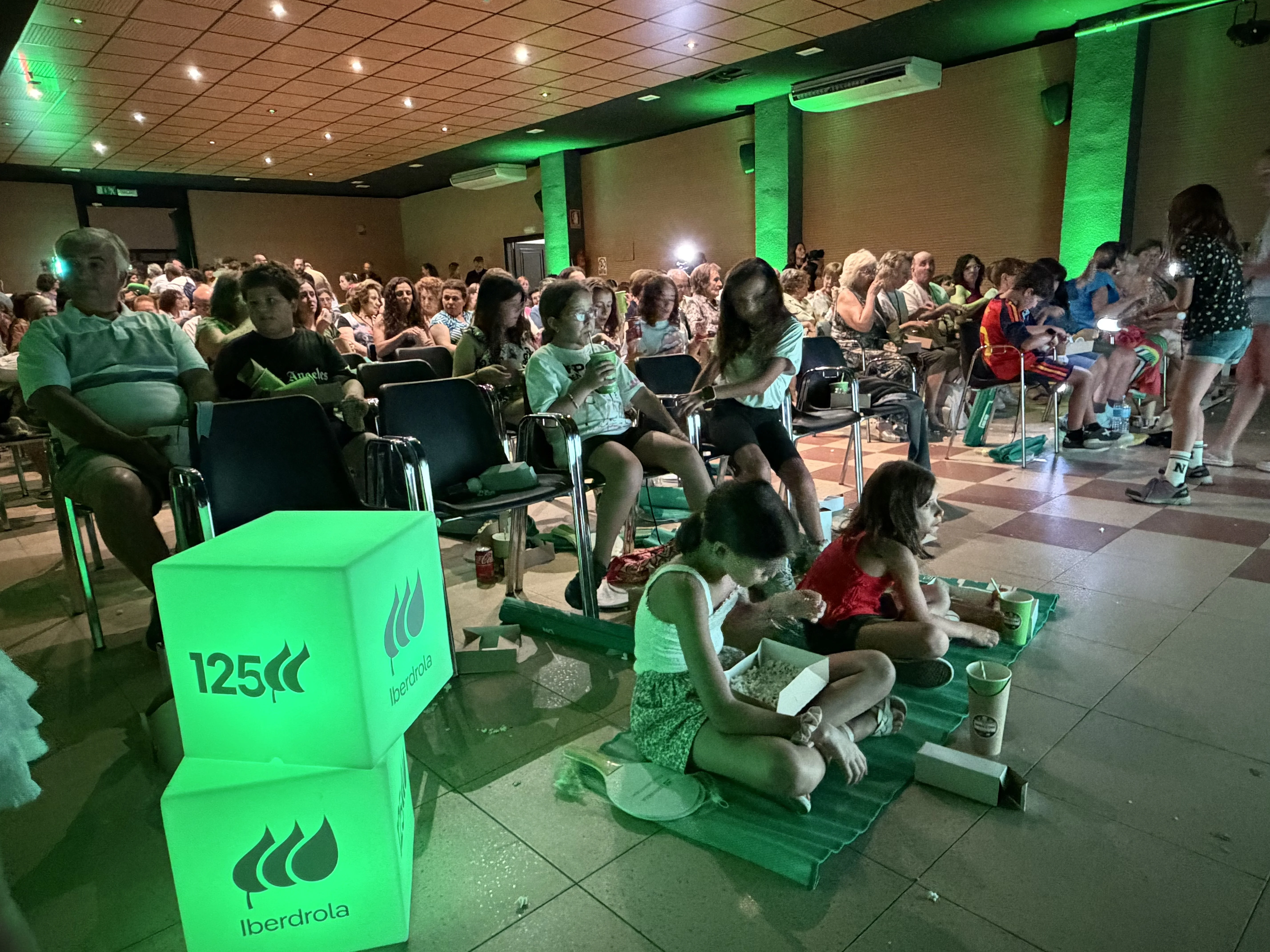 Público asistiendo a una sesión de cine de verano en un espacio interior con iluminación verde de Iberdrola.