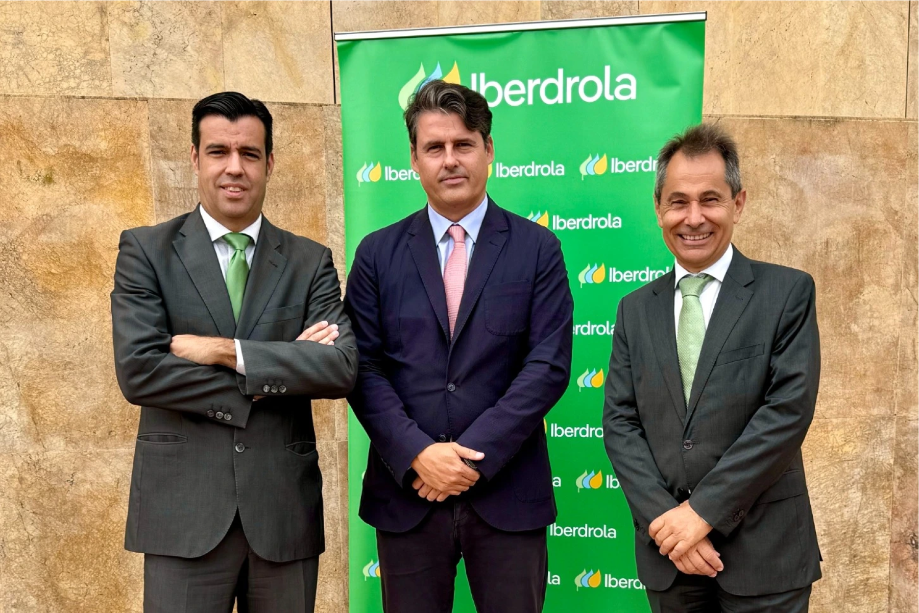 Tres directivos en traje posando frente a fondo corporativo verde de Iberdrola.